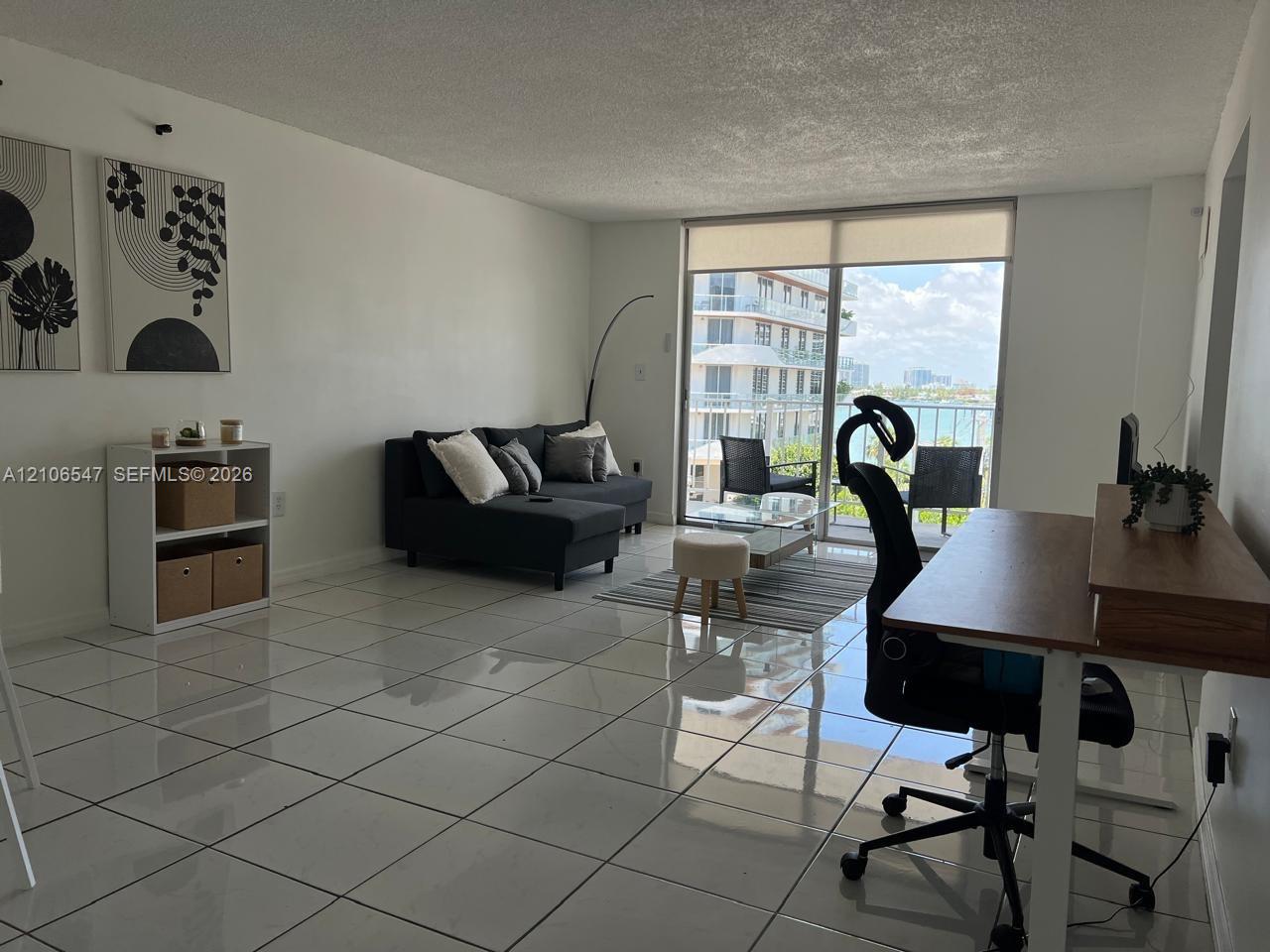 Living area featuring large-format ceramic tile flooring, neutral wall finishes, and floor-to-ceiling glass sliding doors opening to a private balcony