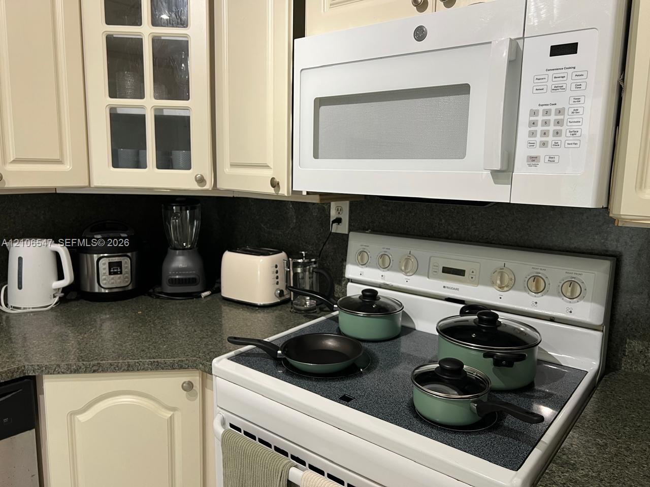 Kitchen featuring off-white raised-panel cabinetry, glass-front cabinet accents, solid-surface countertops, and a white over-the-range microwave
