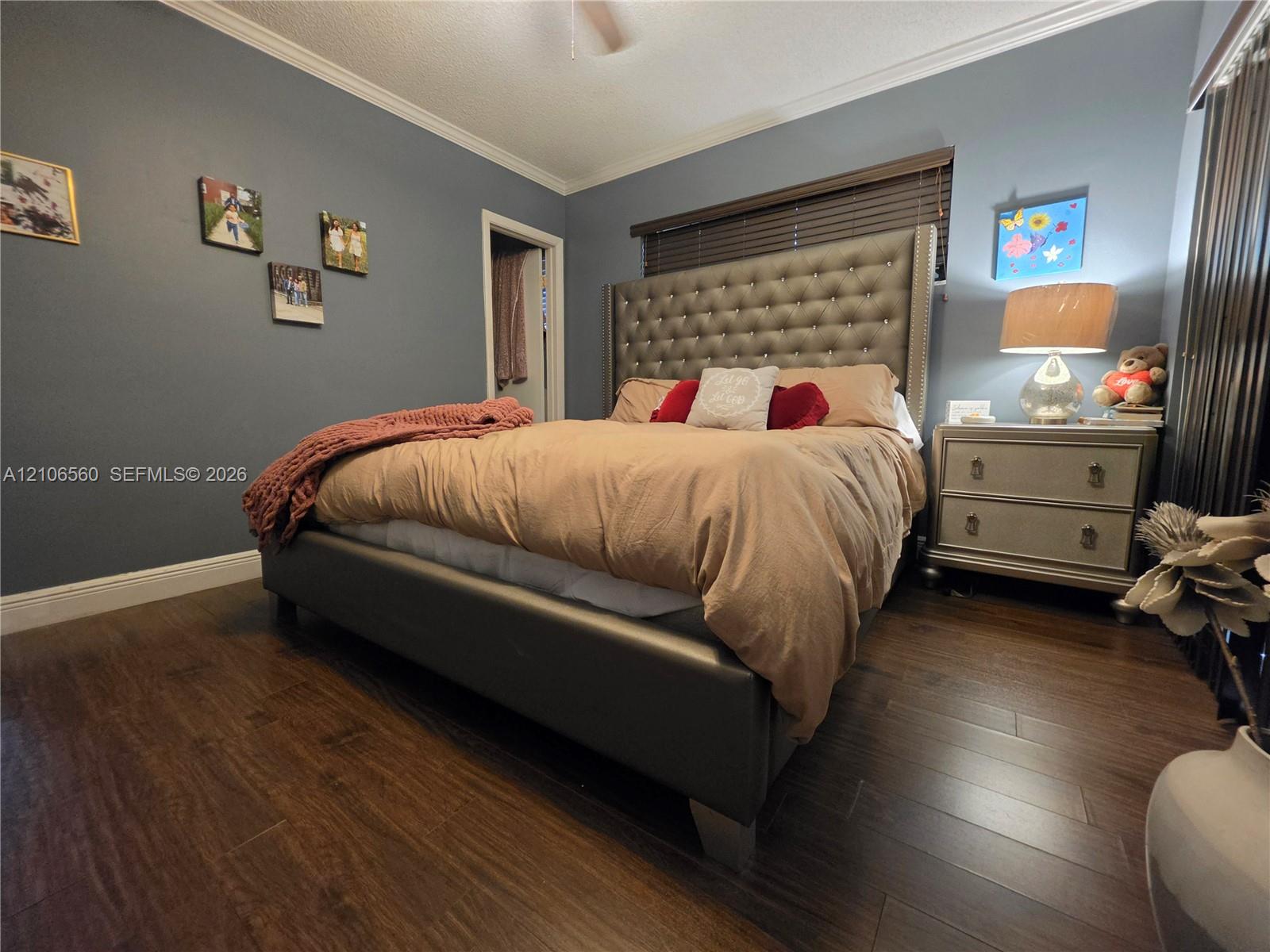 Bedroom featuring dark wood-finish flooring, crown molding, and horizontal slat window blinds