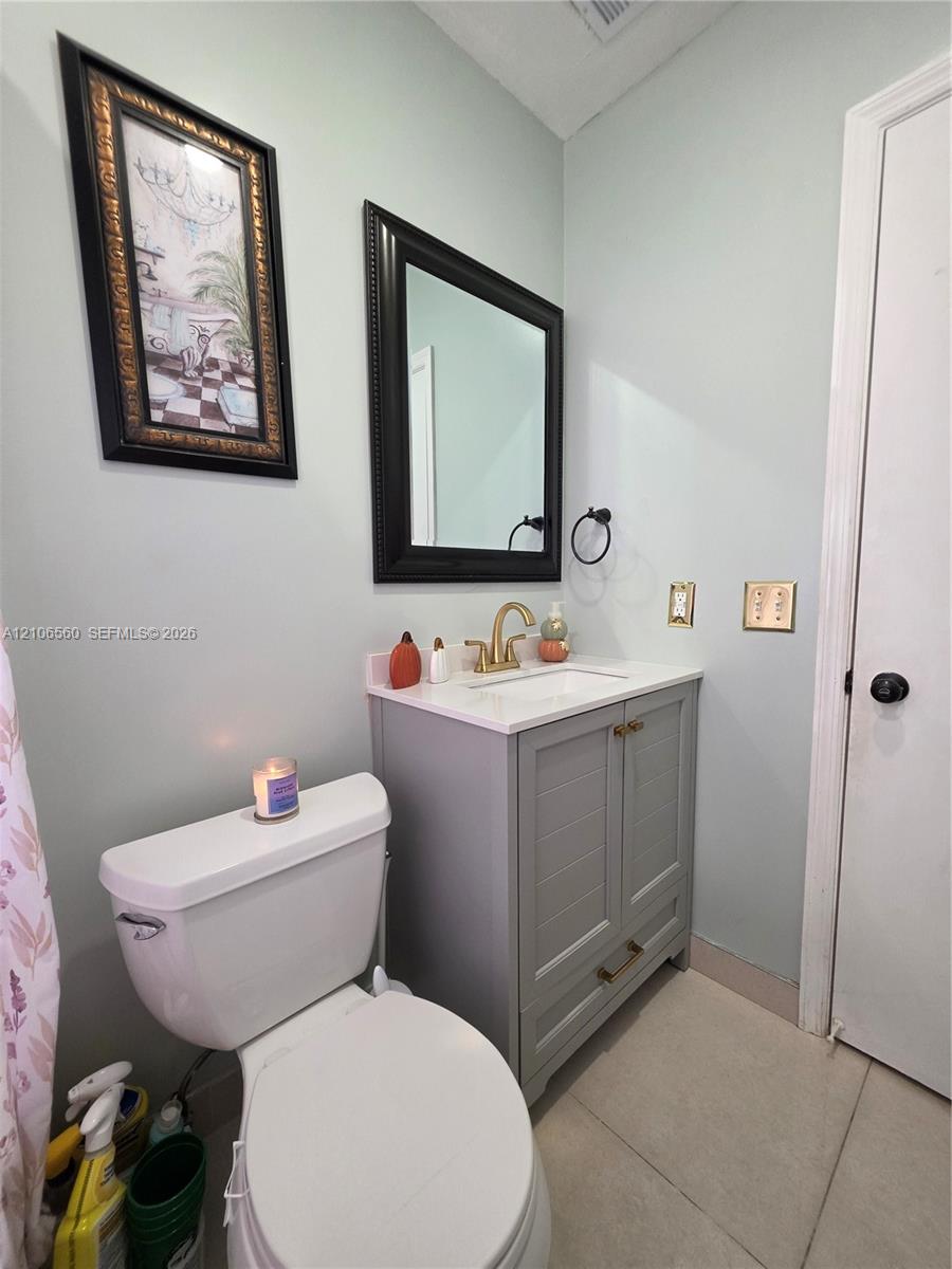 Grey shaker-style vanity with a stone countertop, integrated undermount sink, brushed gold faucet, and a black-framed mirror