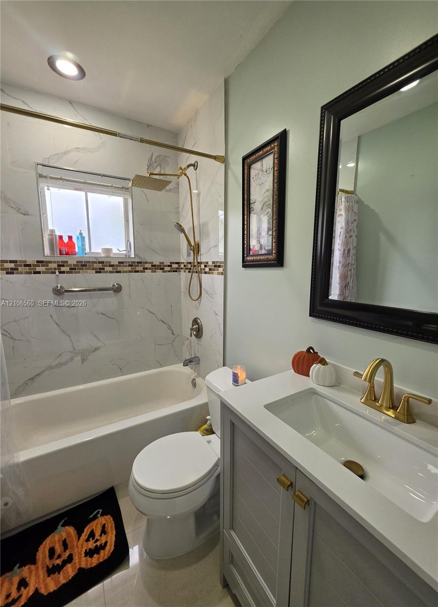 Bathroom featuring a vanity with a white countertop and gold-toned faucet, large-format tile shower surround with decorative mosaic inlay, gold-toned rainfall shower fixture, and recessed lighting