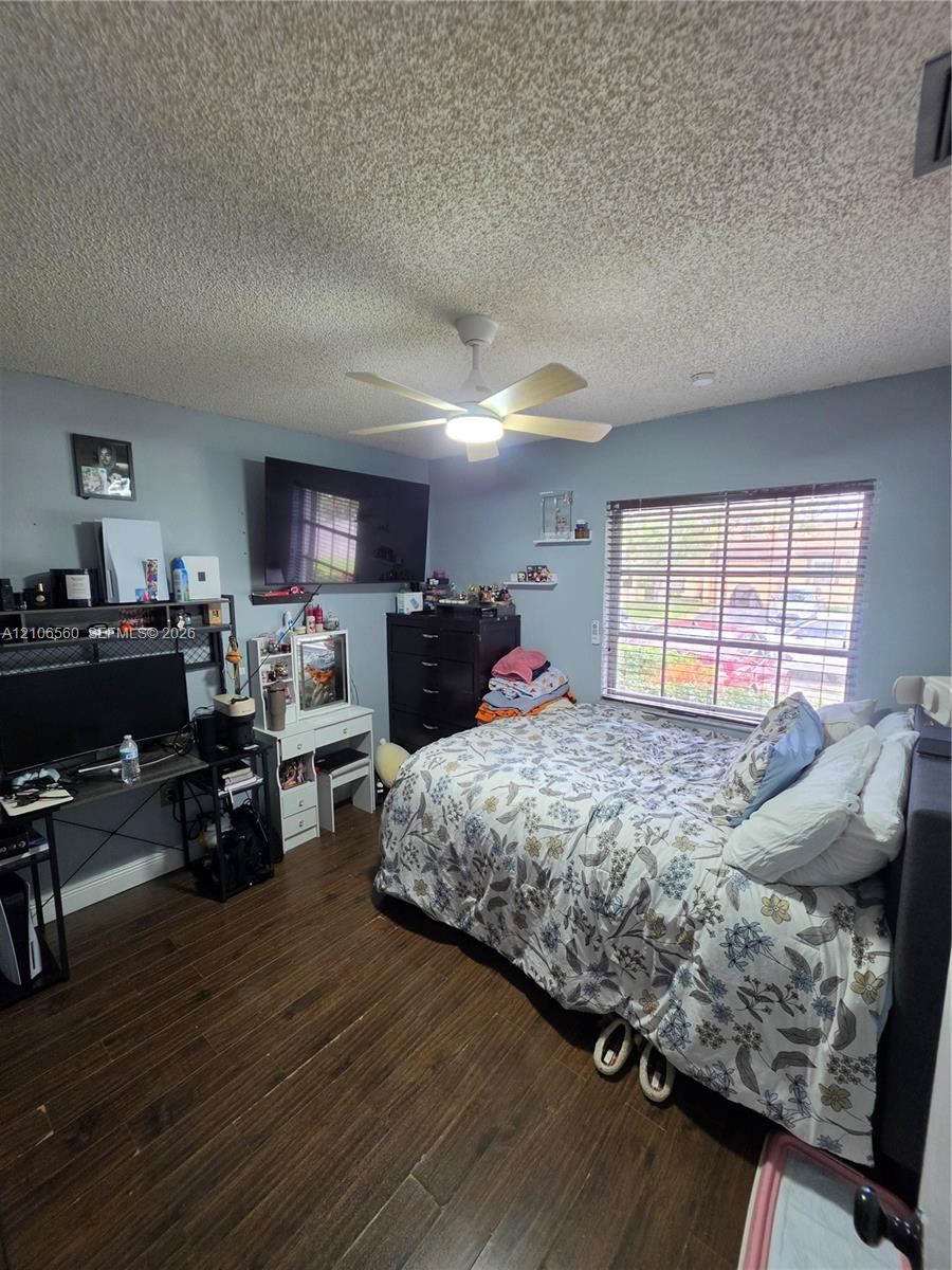 Room featuring wood-finish flooring, a ceiling fan with integrated light, and a window with horizontal blinds