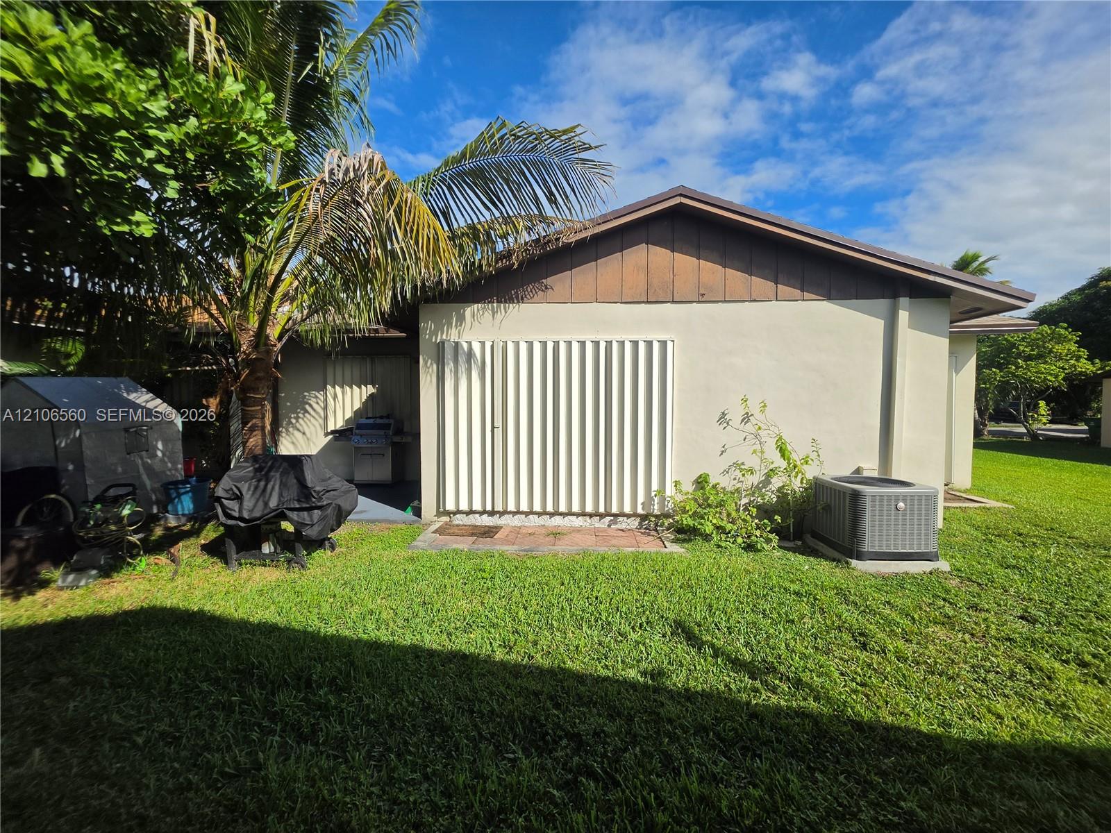 Exterior side profile featuring light-toned stucco walls, vertical wood siding, integrated accordion-style shutters, and a rear lawn