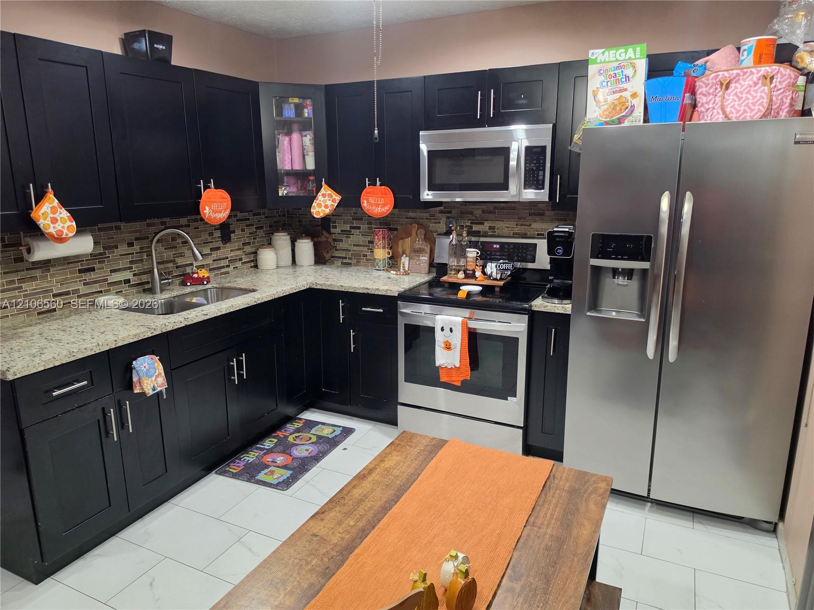 Kitchen featuring dark cabinetry, stone-finish countertops, stainless steel appliances, and a glass-tiled backsplash