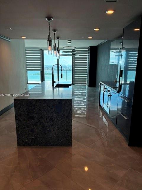 Kitchen featuring a waterfall-edge center island, high-gloss cabinetry, large-format tile flooring, recessed lighting, and pendant fixtures