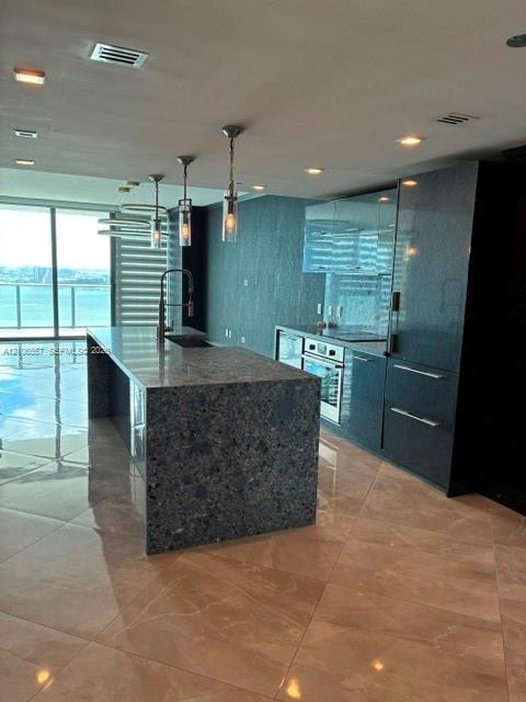 Kitchen featuring a large stone-topped island, high-gloss cabinetry, recessed ceiling lighting, glass pendant fixtures, and oversized tile flooring