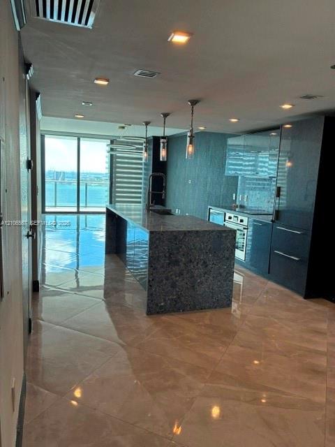 Modern kitchen featuring high-gloss cabinetry, stone-surfaced kitchen island, tile flooring, built-in stainless steel appliances, and ceiling-mounted pendant lighting