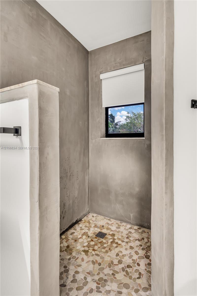 Shower enclosure featuring cement-finish walls, a river rock stone floor, recessed window, and matte black hardware