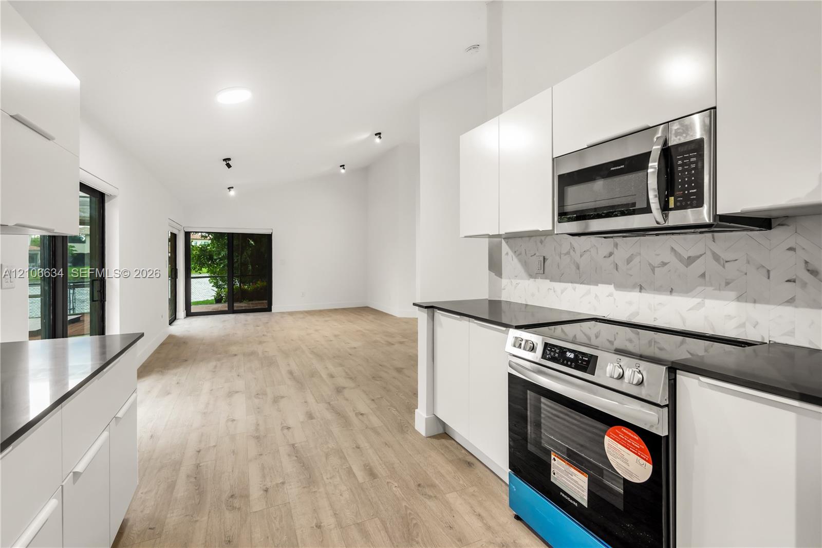 Modern kitchen featuring flat-panel white cabinetry, dark stone countertops, stainless steel appliances