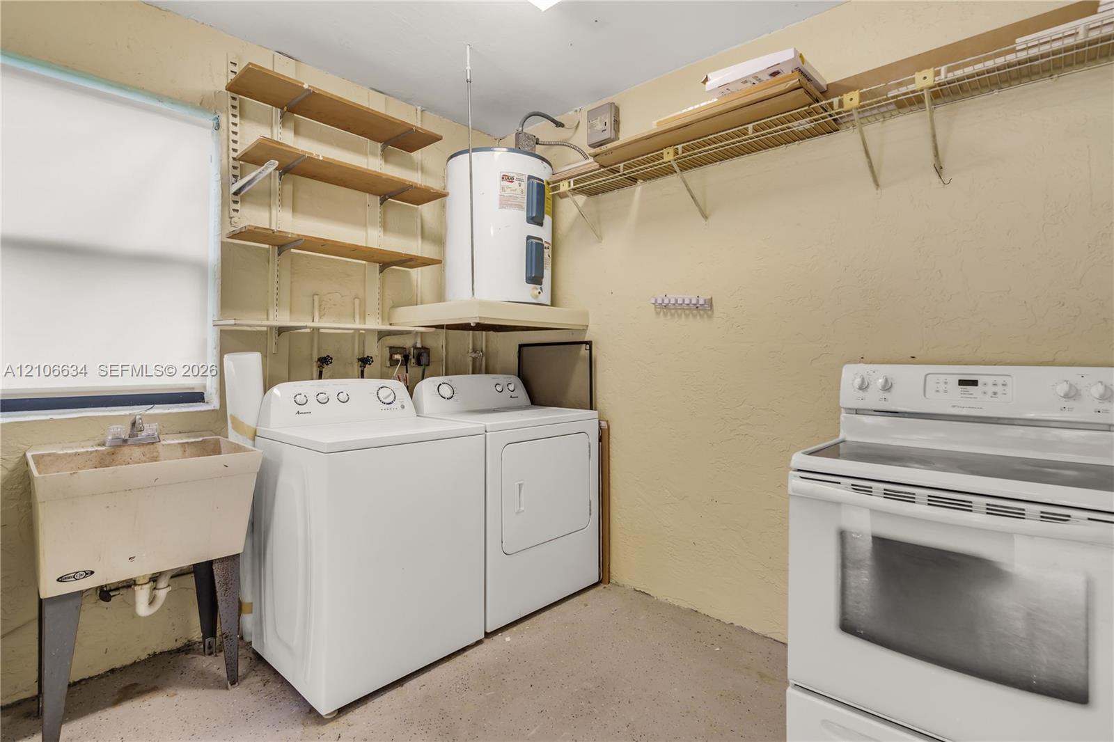 Utility room featuring washer and dryer, a utility sink, wall-mounted shelving, water heater (Stove Range/Oven is no longer there)
