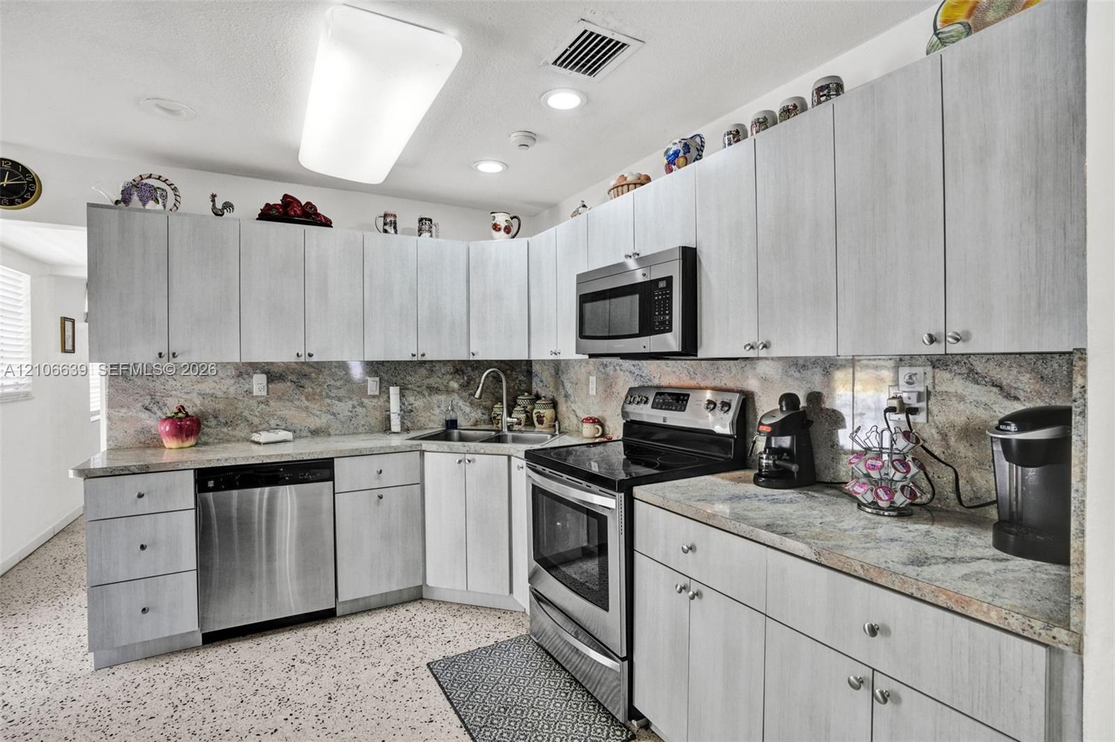 Kitchen featuring light-toned cabinetry, natural stone countertops with matching backsplash, stainless steel appliances, and integrated recessed lighting