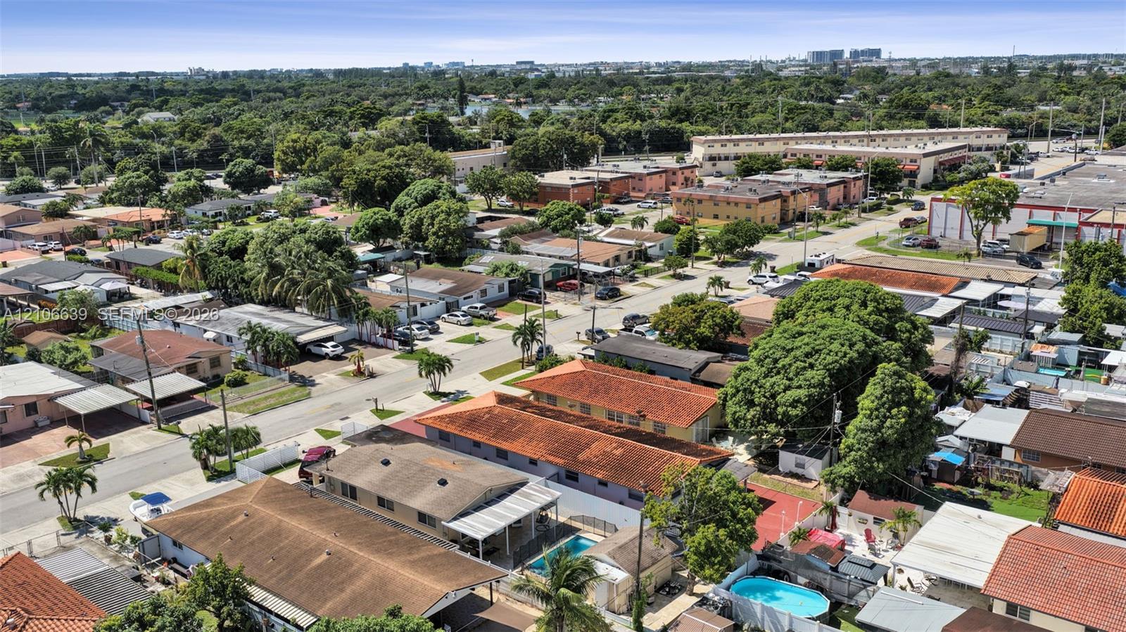 Aerial perspective of a residential neighborhood featuring paved street infrastructure, mature canopy trees, various single-story residential dwellings, and private swimming pools