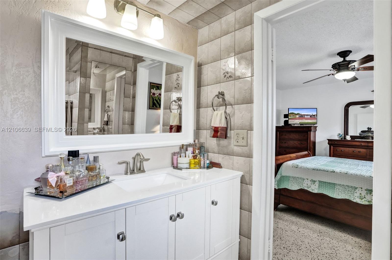 Bathroom vanity with white cabinetry, solid surface countertop, rectangular undermount sink, three-light fixture, and framed wall mirror, accompanied by tiled walls