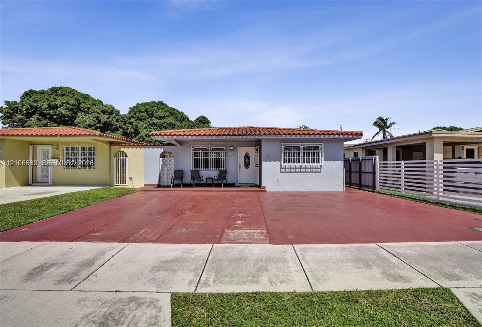 Single-story exterior featuring a clay tile roof, stucco finish, gated front entryway, and a wide paved driveway