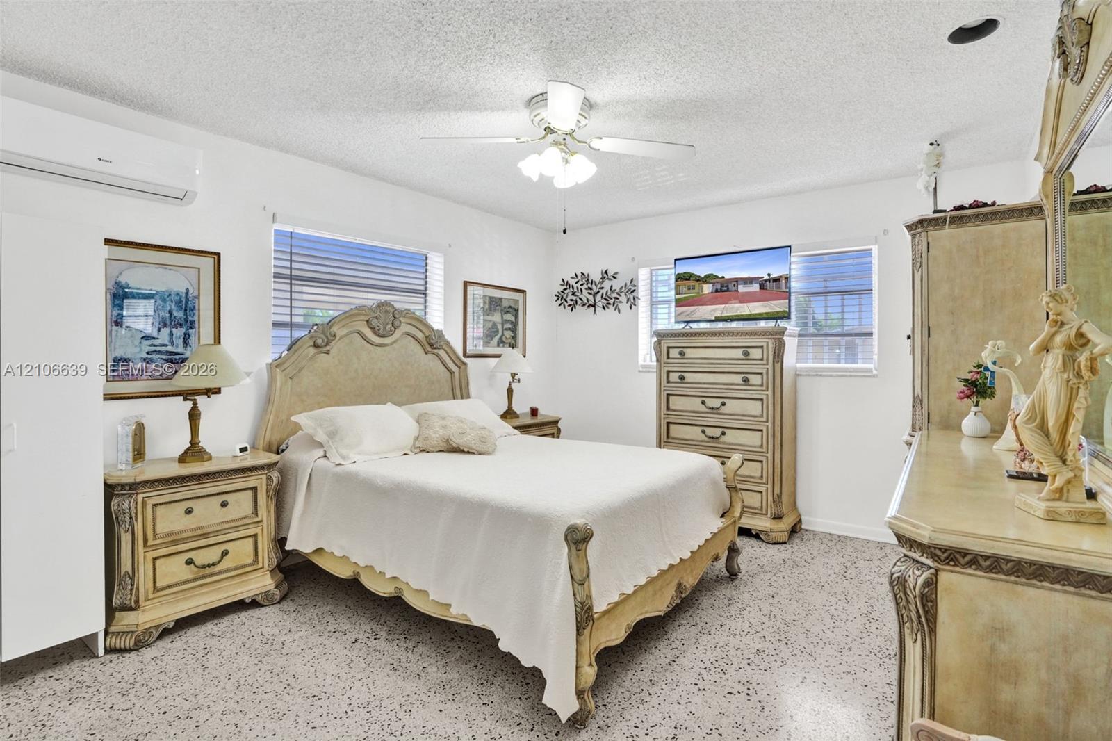 Interior space featuring white walls, terrazzo flooring, a multi-blade ceiling fan with integrated lighting, and a wall-mounted ductless air conditioning unit