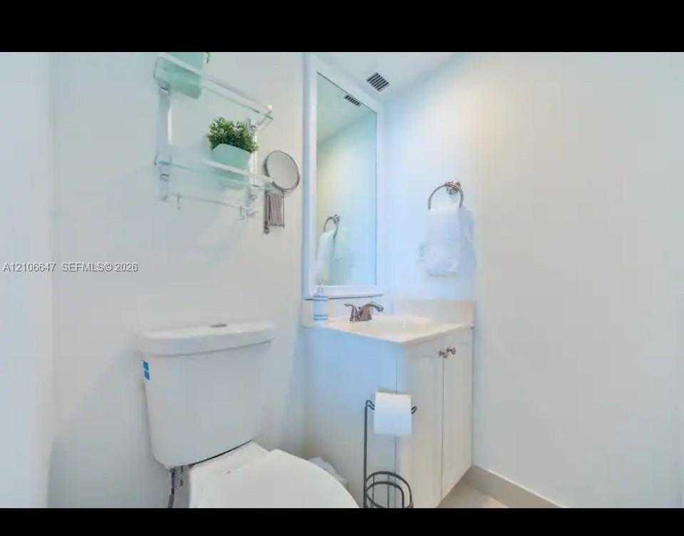 Bathroom featuring a white vanity cabinet with an integrated sink, polished metal faucet, wall-mounted mirror, and wall-mounted glass shelving unit