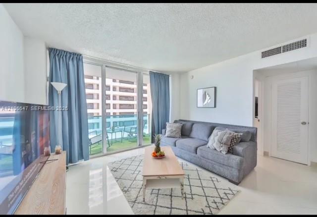 Living area featuring expansive floor-to-ceiling glass sliding doors, private balcony, neutral large-format tile flooring, and a louvered closet door