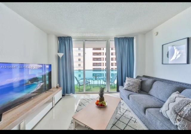 Floor-to-ceiling glass panel windows, sliding glass door, white tile flooring, and a private balcony with glass railing