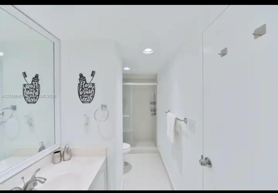 Bathroom featuring a large vanity mirror, solid-surface countertop with an integrated sink, polished chrome faucet, recessed ceiling lighting, and a walk-in shower enclosure