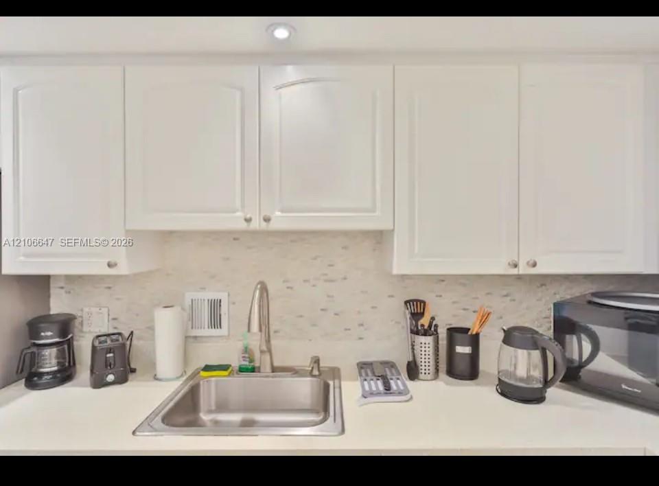White shaker-style cabinetry, solid-surface countertop, stainless steel undermount sink, gooseneck faucet, and mosaic tile backsplash