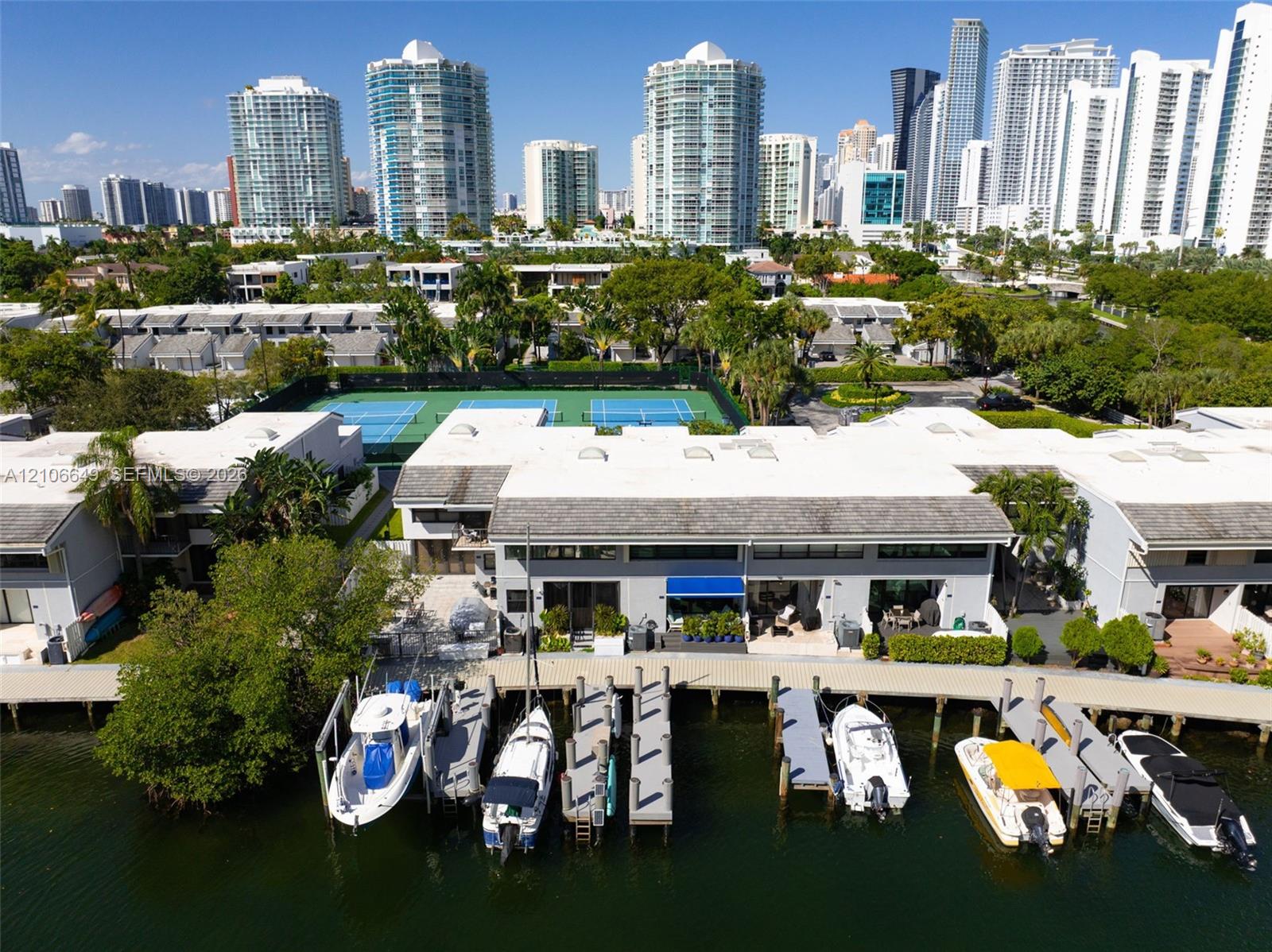 Waterfront residential complex featuring private boat slips, hardscaped docks, a multi-court tennis facility, and expansive coastal surroundings