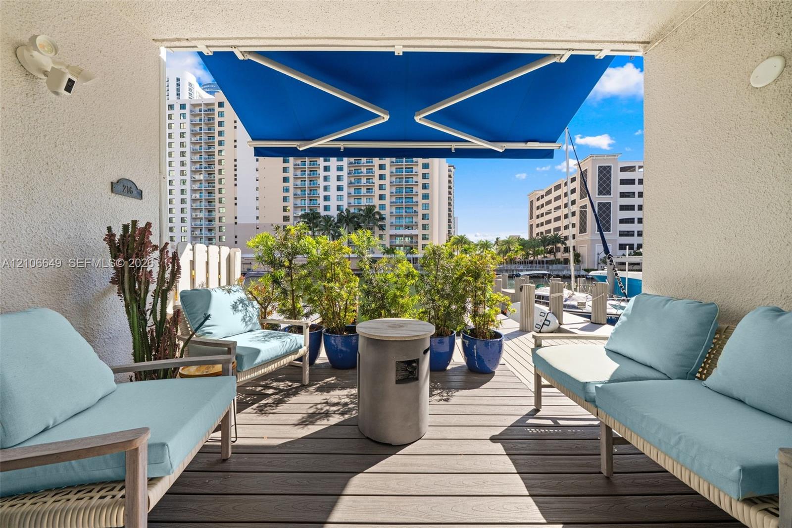 Covered balcony featuring wood-finish composite decking, a retractable fabric awning, and integrated wall-mounted lighting