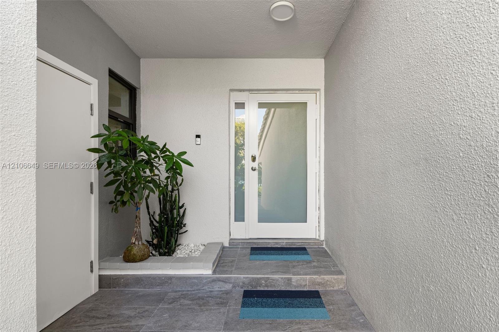 Entryway featuring a white door with a frosted glass panel, recessed ceiling lighting, textured wall finish, grey tiled flooring, and a built-in stone planter
