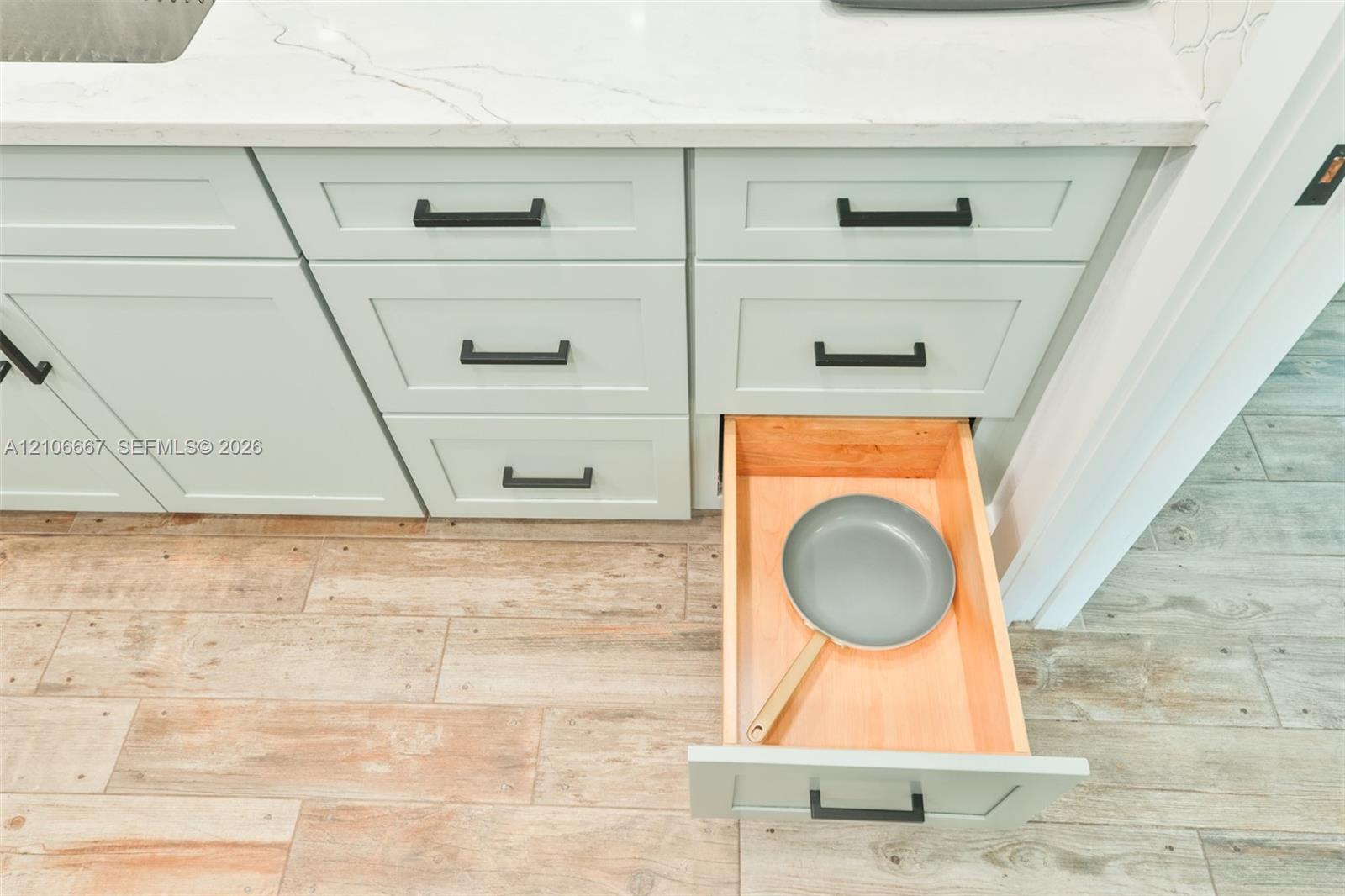 Light-toned shaker-style cabinetry with matte black hardware, stone-finish countertops, and wood-finish tile flooring