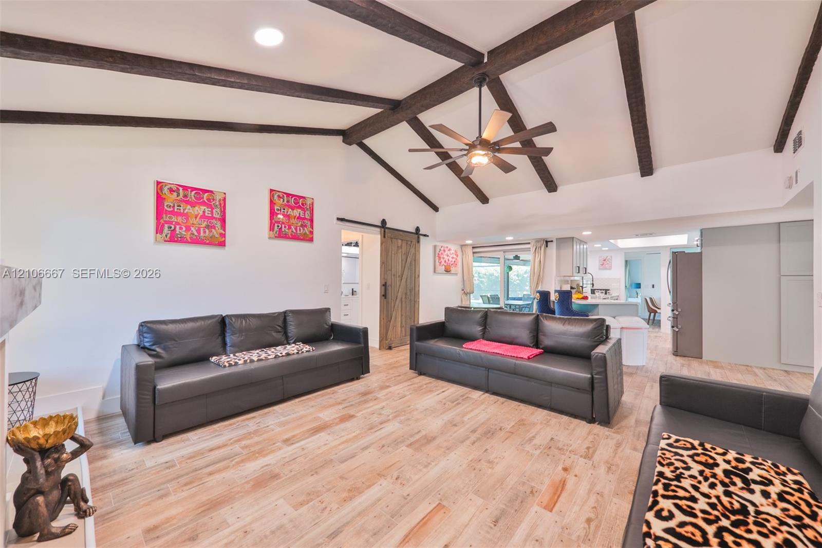 Vaulted ceiling with exposed decorative wood beams, wood-finish tile flooring, and sliding barn door hardware