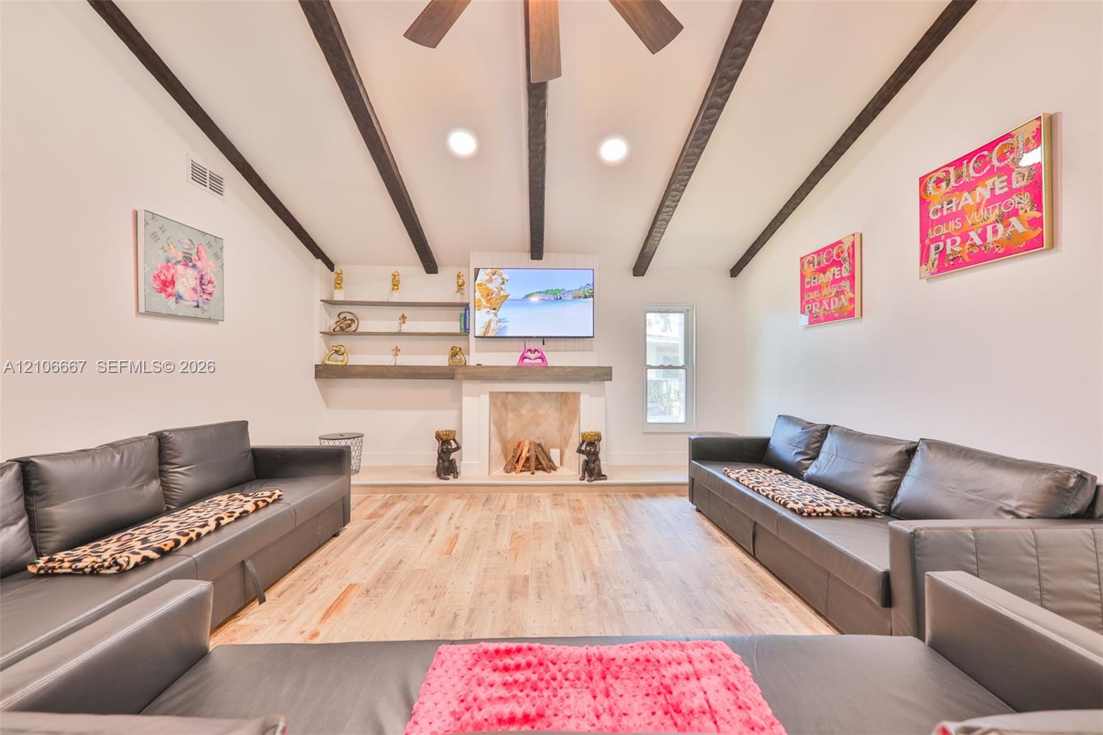 Vaulted ceiling featuring exposed dark wood beams, wood-finish flooring, fireplace with a decorative mantel, and built-in wall shelving