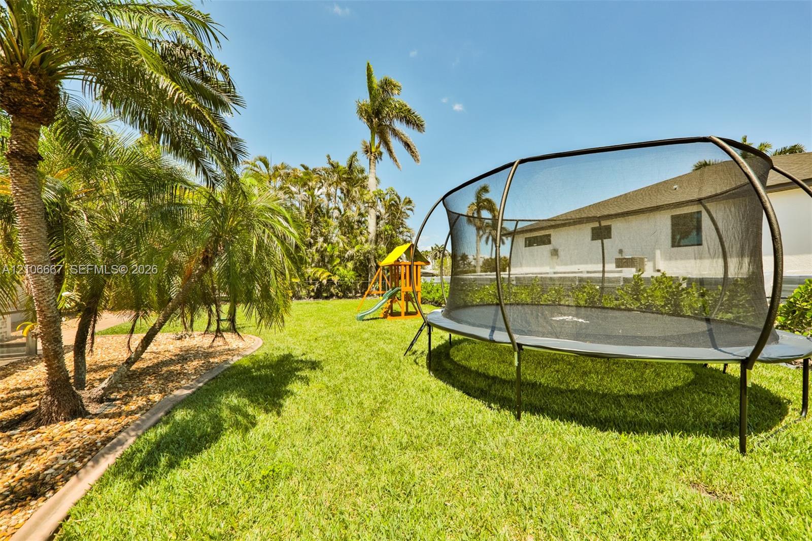 Fenced backyard featuring a manicured lawn, mature palm trees, and perimeter landscaping