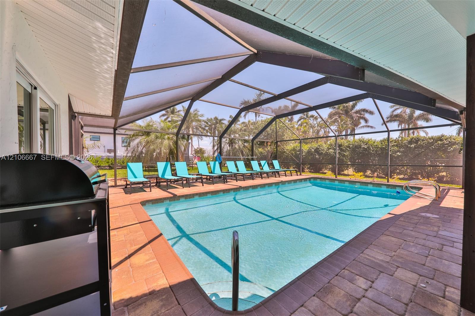 Screened-in pool enclosure featuring paver decking, a built-in pool with metal ladder, and a covered patio area