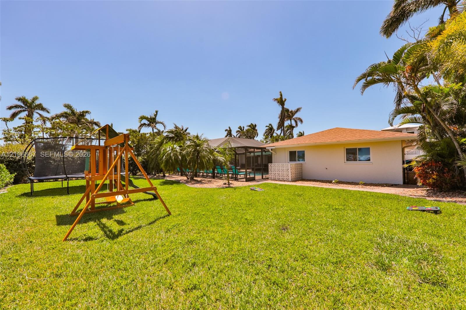 Expansive backyard featuring a manicured lawn, established palm trees, a screened-in lanai, and an exterior masonry privacy wall