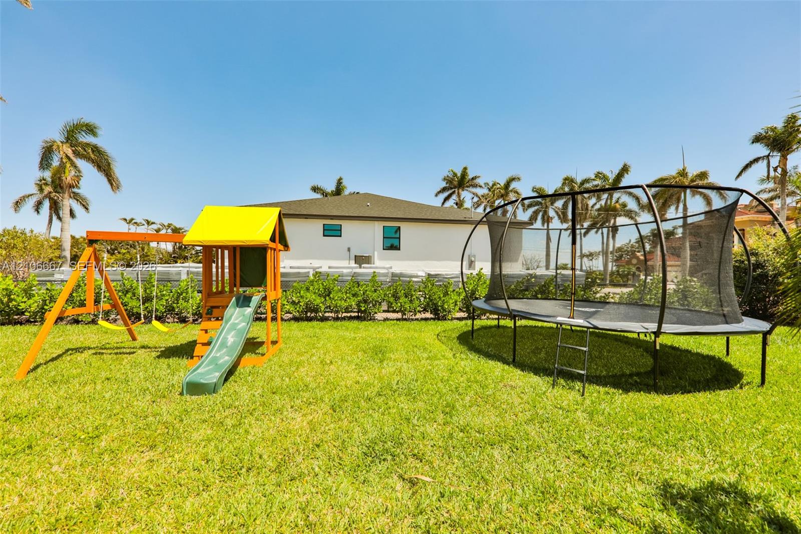 Expansive backyard featuring a level grass lawn, perimeter shrubbery, and mature palm trees