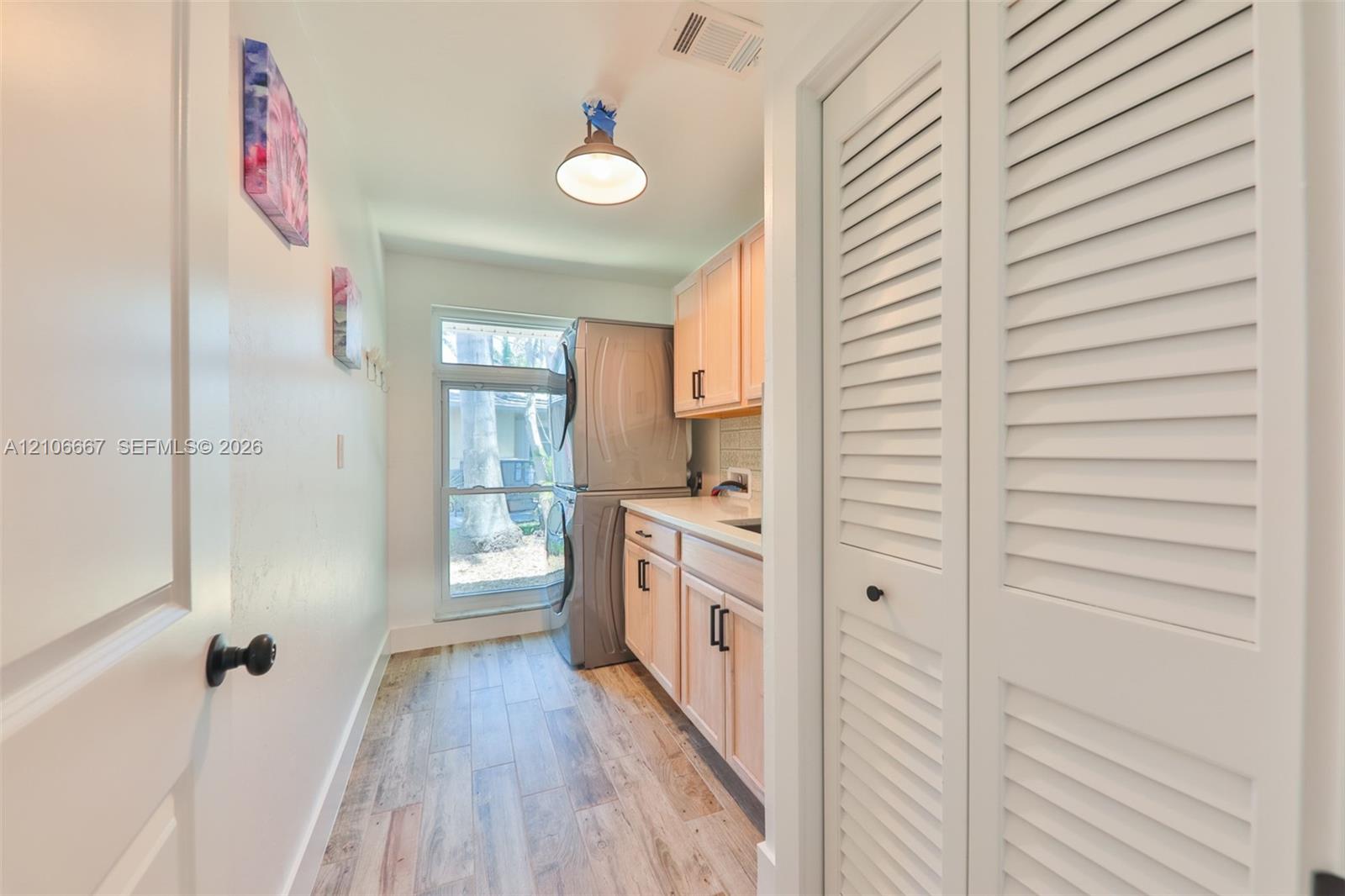 Utility space featuring wood-finish flooring, light-toned cabinetry, a solid-surface countertop, a full-height louvered closet door, and a pendant light fixture