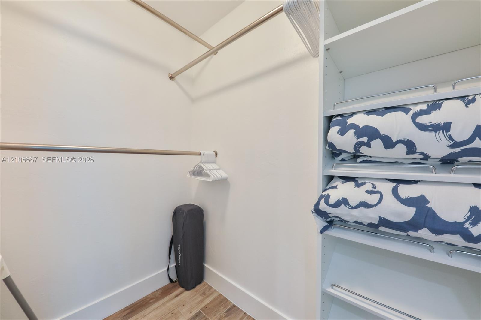 Walk-in closet featuring white built-in shelving, adjustable metal clothing rods, and wood-finish flooring