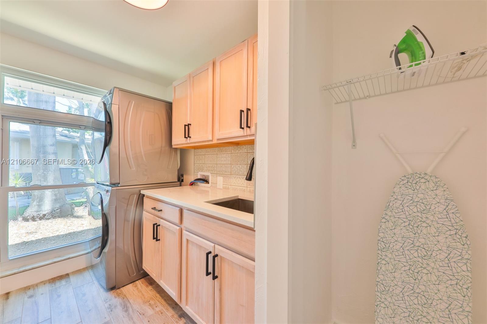 Utility room featuring light-finish cabinetry, a white countertop with an integrated sink, a ceramic tile backsplash, and wood-finish flooring
