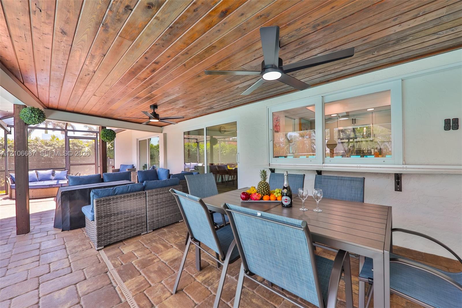 Covered patio featuring a wood-plank ceiling, paver flooring, dual ceiling fans, and an exterior pass-through window