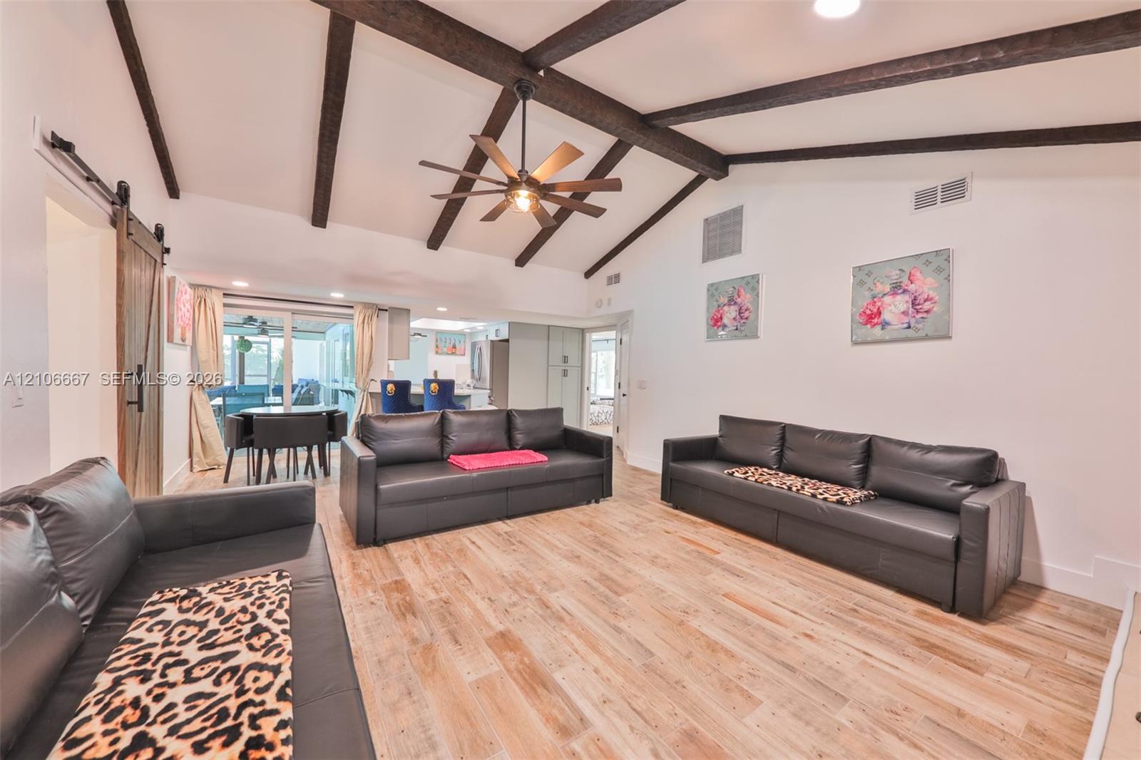 Vaulted ceiling featuring exposed decorative wooden beams, wood-finish flooring, and a central ceiling fan with an integrated light fixture