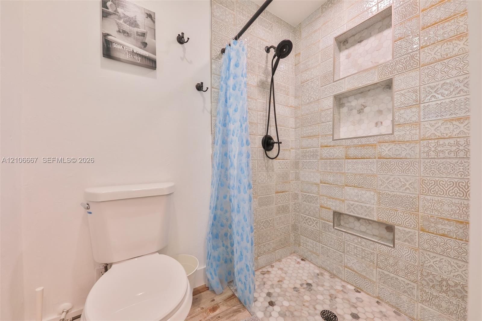 Bathroom featuring textured tile shower walls with three built-in wall niches, a hexagonal mosaic stone shower floor, matte black shower hardware, and a white porcelain toilet