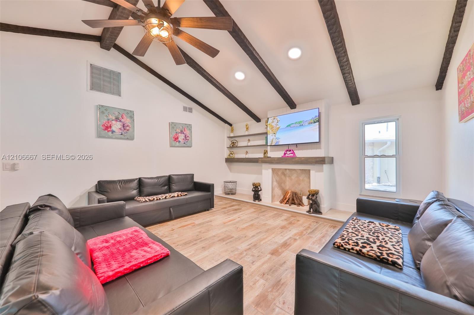 Vaulted ceiling featuring exposed dark wood beams, wood-finish flooring, masonry fireplace with a timber mantel, and built-in shelving