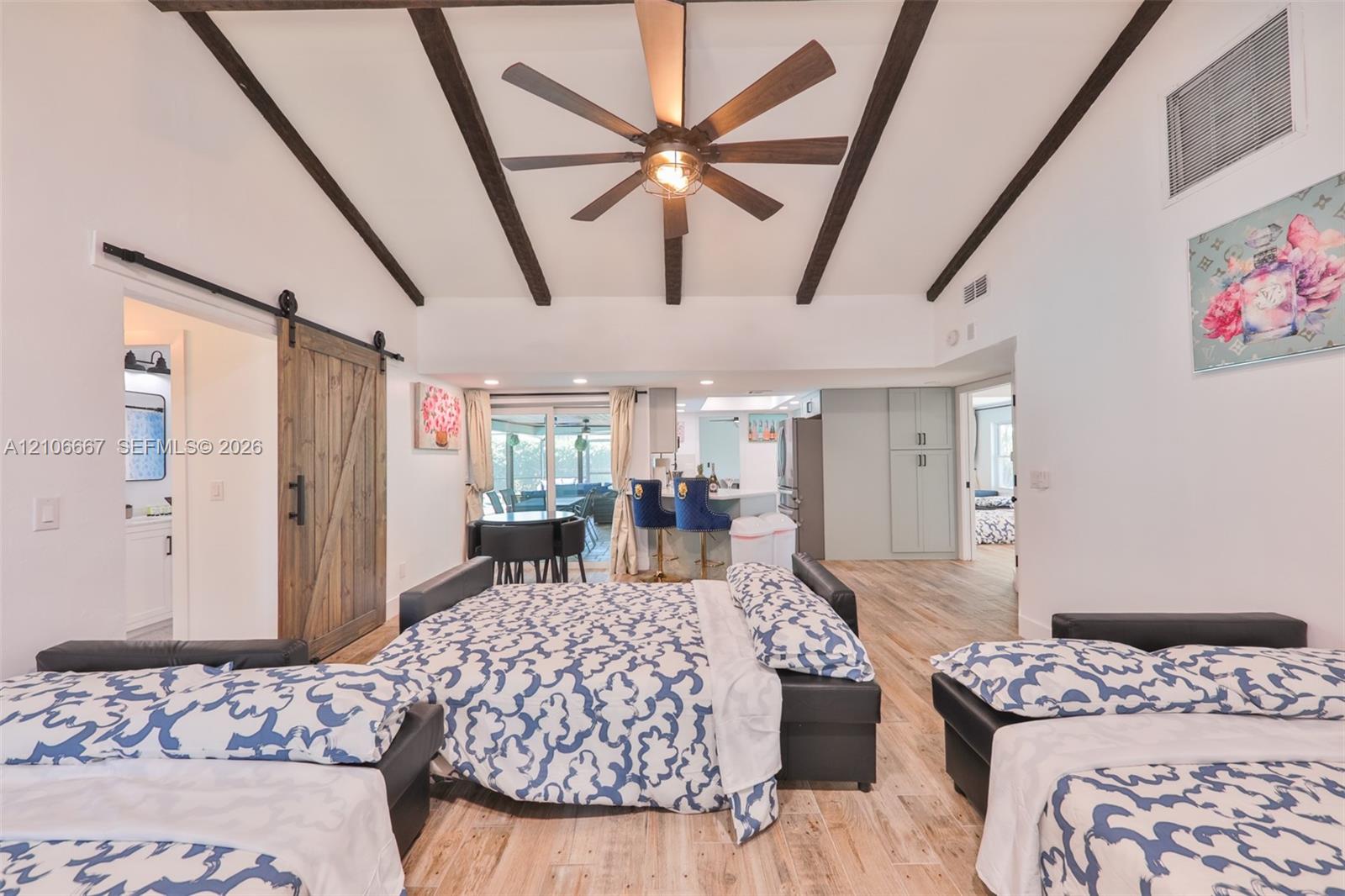 Vaulted ceiling with exposed decorative beams, wood-finish flooring, sliding barn door with matte black hardware, and central ceiling fan with integrated light fixture