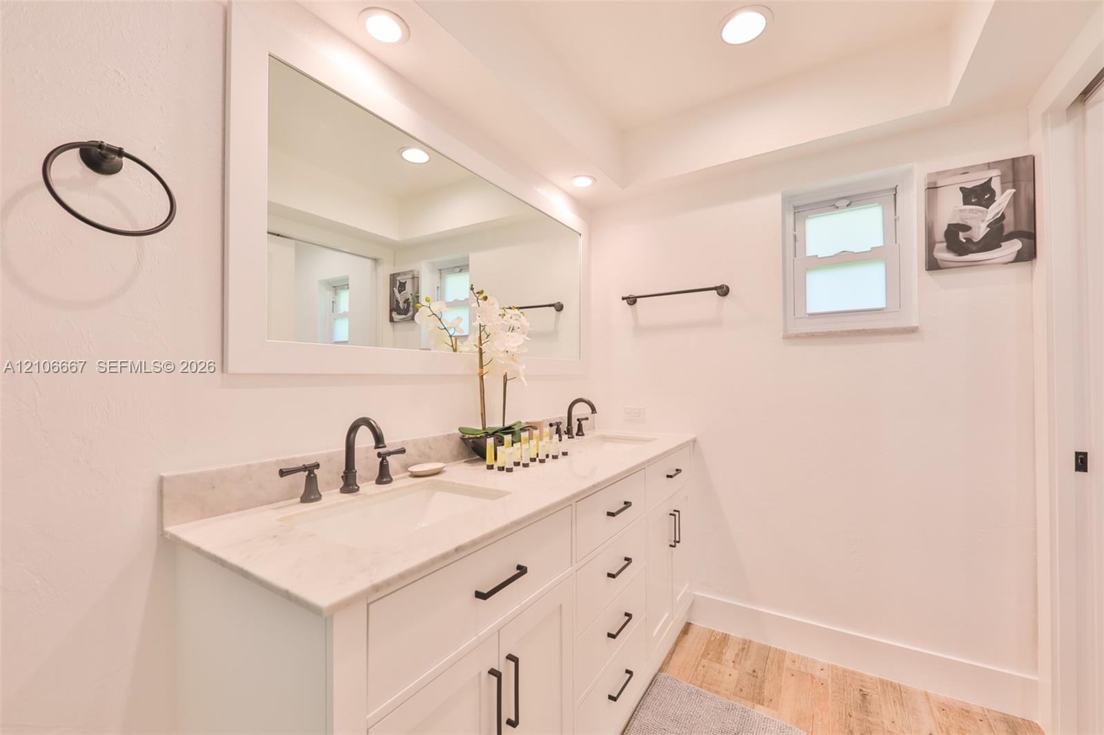 Dual-sink vanity with stone countertop, matte black hardware, integrated cabinetry, wood-finish flooring, and recessed ceiling lighting