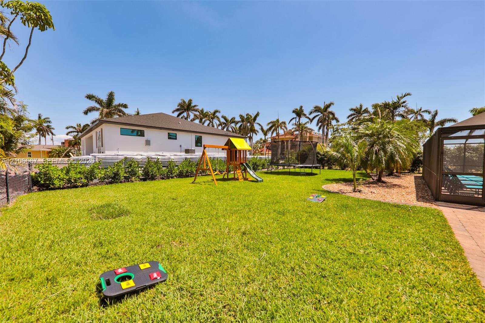 Expansive backyard featuring a manicured lawn, established palm trees, a paver patio, and a screened-in enclosure