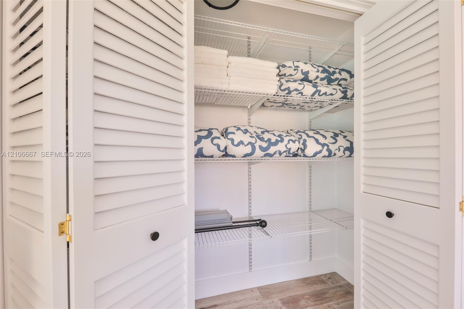 Storage closet featuring white louvered bifold doors, adjustable wire shelving, and wood-finish tile flooring