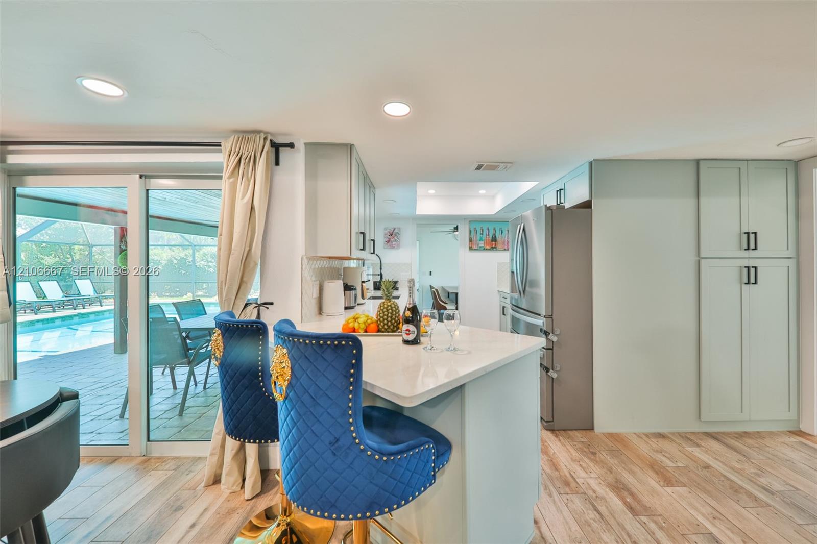 Kitchen featuring a quartz-topped island, light-toned cabinetry, stainless steel refrigerator, recessed lighting, and wood-finish flooring