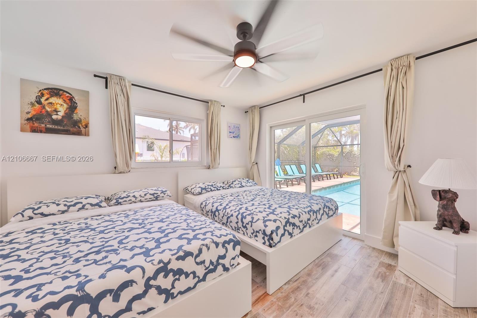 Room featuring wood-finish flooring, a multi-blade ceiling fan with integrated lighting, and sliding glass doors providing access to a screened-in pool enclosure