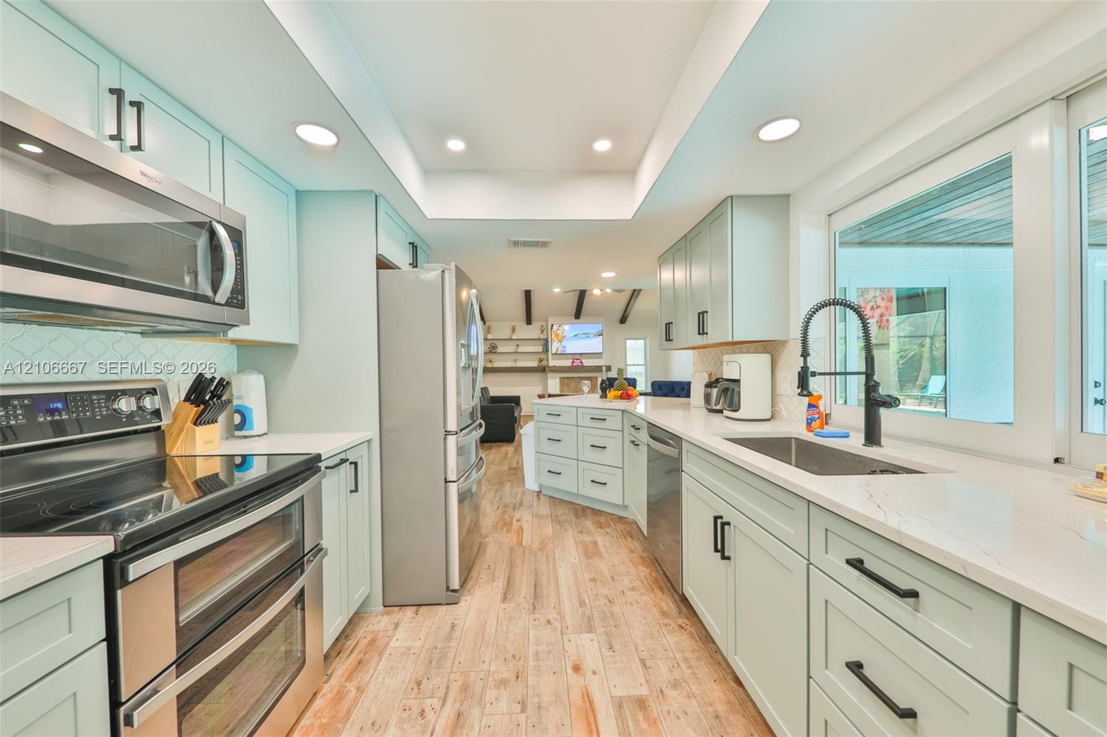 Kitchen featuring light-toned cabinetry, stainless steel appliances, quartz countertops, wood-finish flooring, and recessed lighting