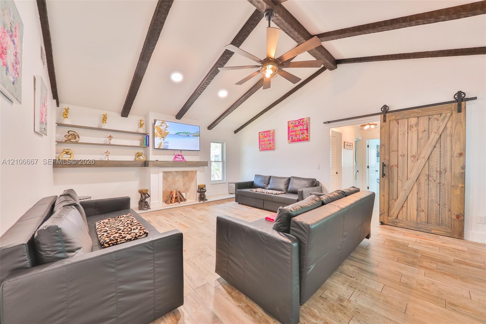 Vaulted ceiling featuring exposed wood beams, wood-finish flooring, fireplace with stone surround, custom built-in shelving, and sliding barn-style door
