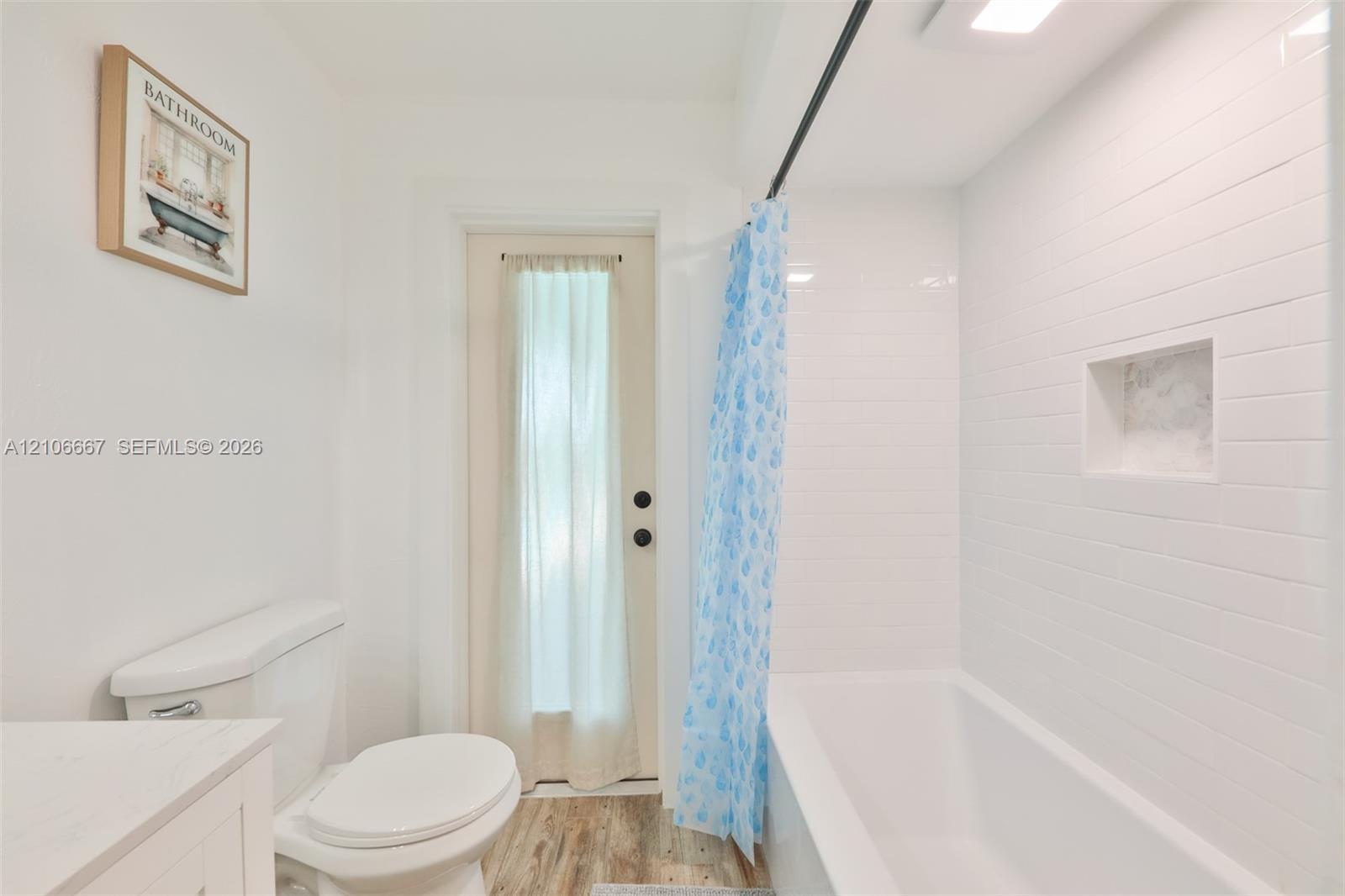 Bathroom featuring a tub with white subway tile surround, built-in recessed wall niche, wood-finish flooring, and a single-door exterior entry